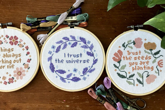 Three finished cross stitch in hoops with threads around them