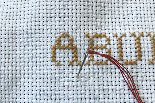 An image showing a needle and thread going through aida fabric to start stitching